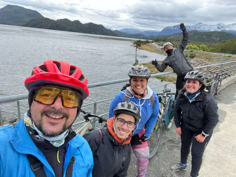 Cinco riders con casco se sacan una selfie junto al lago, con los cerros nevados detrás